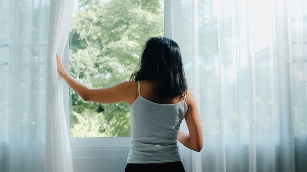 mujer abriendo la cortina para ahorrar energía eléctrica en el hogar